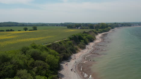 Scenic-aerial-view-of-Baltic-sea-shoreline-in-Germany,-flying-forward-lowering-down-to-tourist-beach,-day
